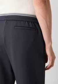 Jūrų pajėgų sportiniai kelnaičiai su lygiu paviršiumi, turintys užpakalinę kišenę ir elastingą juosmenį su pilkų akcentų. Prisegtas modelis.