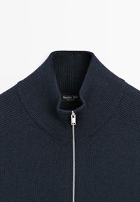 Pull en maille côtelée bleu marine avec un col montant et une fermeture éclair argentée à l'avant, affichant l'étiquette de la marque Massimo Dutti à l'intérieur du col.