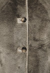 Manteau en fausse fourrure grise avec une texture douce, comportant trois boutons ronds à finition brillante et un doublure lisse le long des bords.