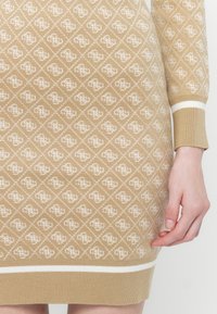 Rochie tricotată în bej cu o textură în carouri albă, având manșete cu tricot diferit și o margine inferioară solidă albă.