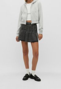 Sudadera gris corta, blusa blanca ajustada, falda de mezclilla negra con pliegues y zapatos negros con calcetines blancos. Diseño minimalista, sin patrones.