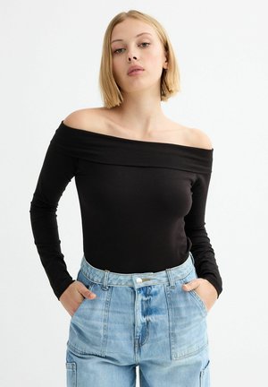 Top negro de manga larga y off-the-shoulder con un diseño ajustado, combinado con unos vaqueros de mezclilla de cintura alta en azul claro que cuentan con bolsillos y cierre de botón.