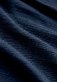 Tissu côtelé bleu foncé avec texture tricotée visible et plis doux créant des ombres délicates.