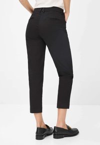 Pantaloni neri a vita alta, dal taglio cropped, con un design aderente, passanti per la cintura e tasche posteriori. Abbinati a mocassini neri con un accento dorato lucido.