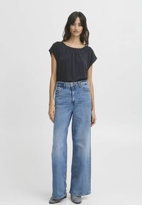 Schwarzes Kurzarmoberteil mit plissiertem Ausschnitt, kombiniert mit hellblauen, weit geschnittenen Jeans mit hoher Taille und klassischer Naht.