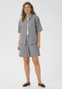 Chemise à manches courtes rayée gris et blanc à boutons, accompagnée d'un short assorti. Tissu léger avec une coupe décontractée. Des ballerines noires complètent le look.