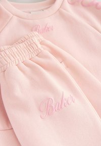 Różowy zestaw dresowy z bawełny składający się z bluzy i spodni, z haftem "Baker" w dopasowanym odcieniu różu. Miękka tekstura, ściągacze w mankietach i elastyczny pas.