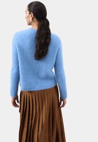 Jasnoniebieski, puszysty sweter z prążkowanymi mankietami, w zestawie z brązową, plisowaną spódnicą. Tekstura swetra jest miękka i puszysta.