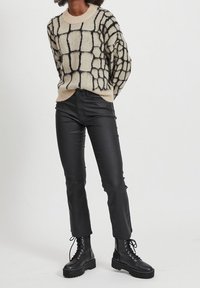 Maglione beige peloso con un motivo a griglia nera, abbinato a pantaloni in pelle nera aderenti e stivali neri con lacci spessi.