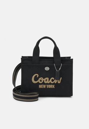 Schwarze Stoffhandtasche mit "Coach New York" in Hellbraun gestickt, mit zwei Griffen, einem gestreiften Schulterriemen und einem kleinen hängenden Anhänger.