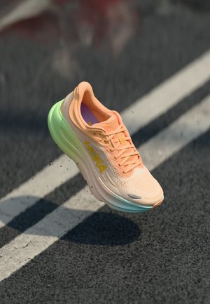Running shoe with a peach mesh upper and green sole. Features a prominent yellow logo, textured lacing, and a cushioned design.