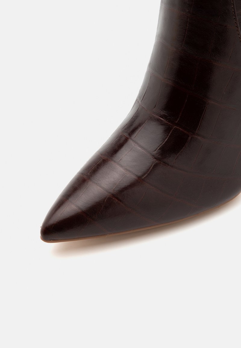 Stivaletto in pelle marrone con punta affusolata e texture in pelle di coccodrillo. Finitura liscia con un leggero lucido, che si restringe alla caviglia.