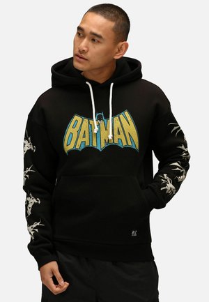 Felpa nera con grafica "BATMAN" in blu e giallo. Presenta un cordino bianco, accenti grafici sulle maniche e tasca a marsupio sul davanti.