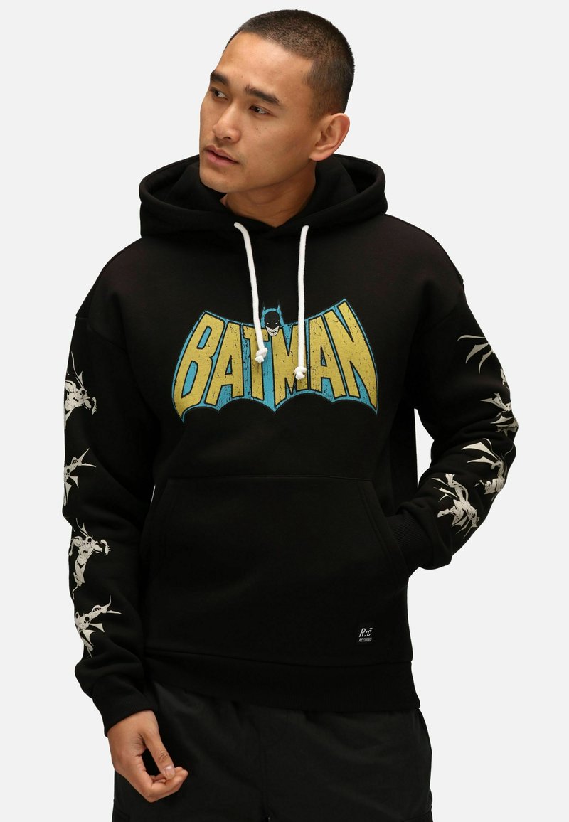 Felpa nera con grafica "BATMAN" in blu e giallo. Presenta un cordino bianco, accenti grafici sulle maniche e tasca a marsupio sul davanti.