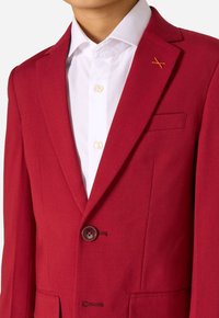 Blazer rosso realizzato in tessuto testurizzato con colletto a rever, chiusura con un bottone marrone e una tasca sul petto sinistro con cuciture arancioni.