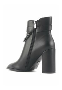 Black leather ankle boot with a pointed toe, side zipper, thick block heel, and decorative chain detail on the upper.
