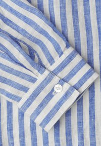 Poignet de chemise à manches longues rayée verticalement bleu et blanc avec un bouton blanc, montrant la texture du tissu et les détails de la couture.