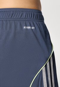 Jūriniai sportiniai šortai iš lengvos medžiagos, su tekstūruota paviršiumi, žaliais krašteliais ir baltu „AEROREADY“ logotipu.