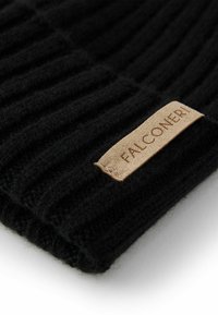 Czarna prążkowana dzianinowa czapka z miękką fakturą. Posiada brązową skórzaną metkę z tłoczonym napisem „FALCONERI” umieszczoną blisko dolnej krawędzi.