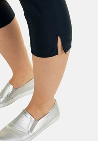 Navy cropped pantalons met een split aan de zoom, gecombineerd met glanzende zilveren instapschoenen met elastische zijpanelen.