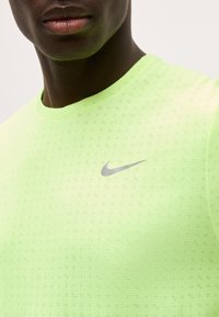 Κοντινό πλάνο ενός ατόμου που φοράει ένα φανελάκι Nike νέον πράσινο με υφή και γκρι λογότυπο Nike στο στήθος.