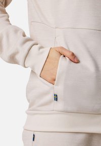 Light beige sweatshirt with a kangaroo pocket, elastic cuffs, and a small Swedish flag accent near the pocket. Soft, textured fabric.