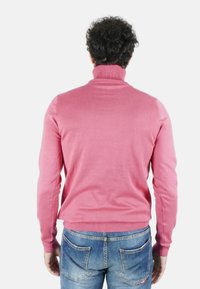 Maglione rosa con collo alto e maniche lunghe, realizzato in materiale morbido, con polsini e orlo a coste, abbinato a jeans blu.