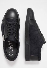 Černé tenisky s hladkým koženým špičkou, vyraženým vzorem na textilních stranách a plochou gumovou podešví, s tkaničkami a stříbrným zipem.