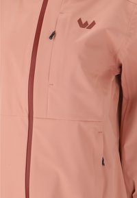 Lys pink kvindelig jakke med lynlås foran, brystlomme og logo accent. Lavet af glat, slidstærkt materiale med kontrast lynlåsdetaljer.