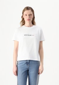 T-shirt bianca in cotone con scollo rotondo e maniche corte. Presenta la scritta in rilievo "MI DISPIACE MA NON MI DISPIACE" sul petto.
