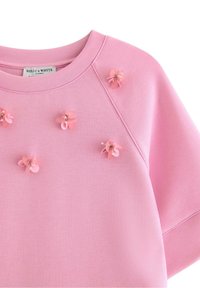 Felpa rosa chiaro con scollo rotondo, maniche corte e applicazioni decorative di fiori di plastica con dettagli di perline sulla parte anteriore.