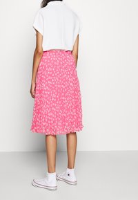 Jupe plissée fleurie rose en tissu léger, ornée de motifs de marguerites blanches. Associée à des baskets montantes blanches et un haut à manches courtes.