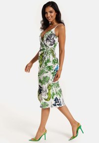 Floral dress featuring green and blue tropical patterns on a white background, with a wrap design, spaghetti straps, and a tie waist.