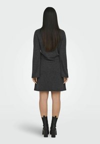 Mörkgrå klänning i mjukt material med långa ärmar och utsvängd nederkant. Svart klumpig klackstövlar kompletterar outfiten.