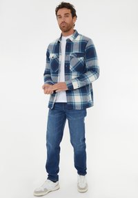 Rutet, blå flannel skjorte med to brystlommer, lagt over en hvid t-shirt; parret med blå jeans og hvide sneakers.
