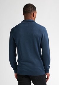 Pulover albastru marin cu mânecă lungă, cu guler tip polo, design ajustat și manșete cu dublură, realizat dintr-un material moale și texturat.