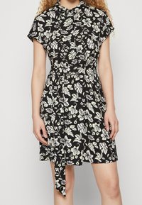 Svart blommig klänning med korta ärmar, bälte i midjan, prydd med vita och gröna blommönster genom hela, mjukt tyg, knälång nederkant.