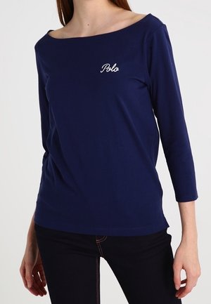 Haut bleu marine à manches longues avec un large col. Présente un logo "Polo" brodé en blanc sur la poitrine. Fabriqué en tissu doux et extensible.