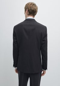 Czarna, dopasowana marynarka z klapami z wycięciem, gładką fakturą, pojedynczym rozcięciem z tyłu i mankietami zapinanymi na guziki, ustawiona na jednolitym tle.