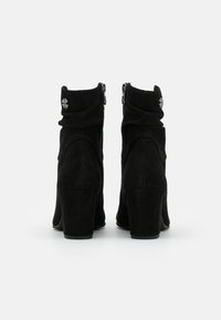 Botines de ante negro con un ligero tacón, que cuentan con un cierre de cremallera y un detalle fruncido en el tobillo. Embellecidos con un acento plateado.