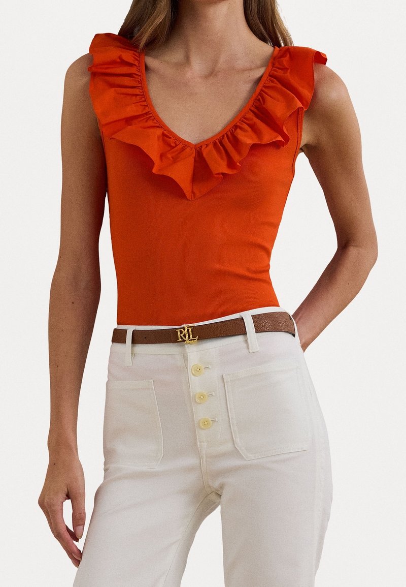 Oranžový volánkový body s výstřihem do V spárovaný s bílými kalhotami s vysokým pasem, které mají čtyři knoflíky, a hnědým páskem s akcentem zlatého loga.