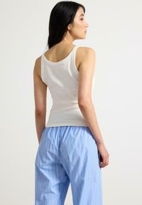 Hvid ribbet tanktop med brede stropper, kombineret med lyseblå stribede pyjamasbukser med elastisk talje og løs pasform.