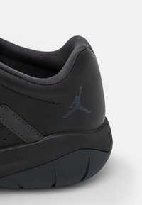 Gros plan du talon d'une chaussure de sport noire avec col rembourré, semelle texturée et logo Jumpman discret sur le côté.