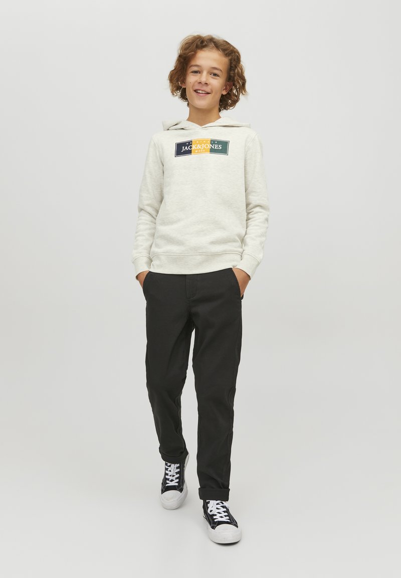 Felpa grigia chiara con logo, tasca a marsupio frontale e cappuccio con cordino; abbinata a pantaloni neri e sneakers nere.