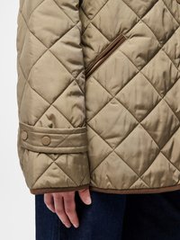 Μπεζ μπουφάν με καπιτονέ υφή και διαγώνιο μοτίβο, καφέ λεπτομέρειες και πλαϊνή τσέπη με φερμουάρ. Οι μανσέτες διαθέτουν κουμπιά snap για ρύθμιση.