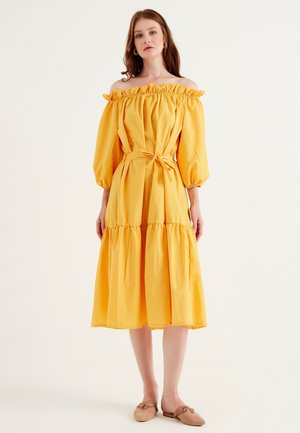 Geel off-shoulder jurk met ruffles aan de halslijn, ballonmouwen, een ceintuur op de taille en een gelaagde rok; van katoen, met een soepele textuur.