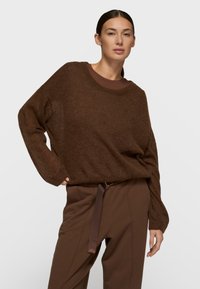 Pull tricoté marron, duveteux, à manches longues et col rond, assorti d'un pantalon marron avec devant plat et ceinture à détails.