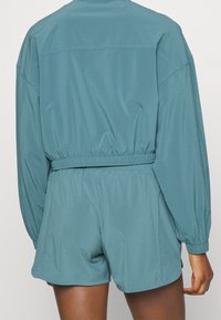 Turkisblå letvægts joggingdragt med indsnøret talje, lange ærmer og elastiske manchetter. Shorts har en løs pasform og blød tekstur.