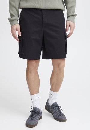 Black cargo shorts with side pockets, made from a durable fabric. Worn with grey sneakers and white crew socks, displayed against a white background.