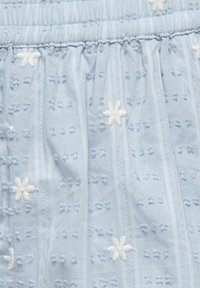 Tissu bleu clair avec des motifs floraux blancs brodés et petits trous de broderie anglaise en rayures verticales.